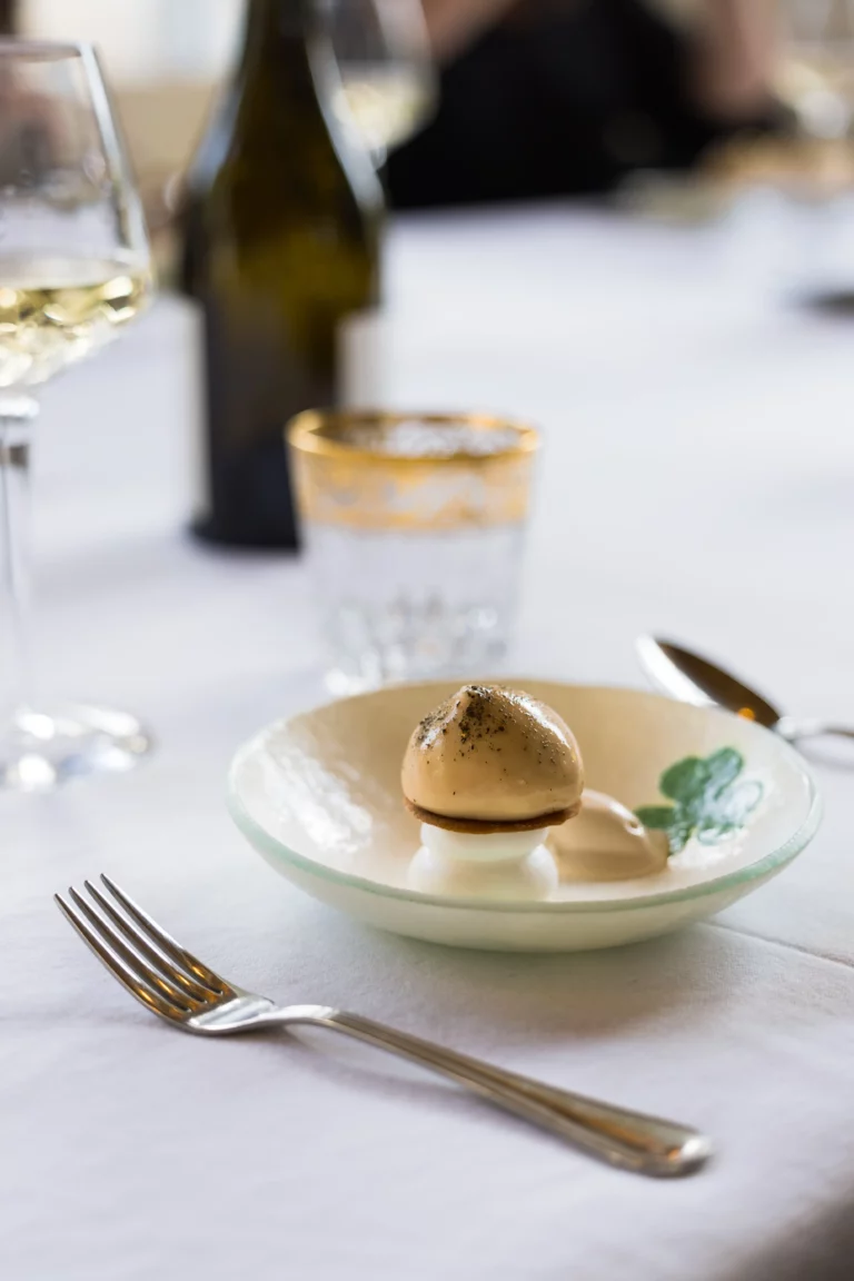 Dessert gastronomique dressé avec finesse sur une assiette en céramique artisanale, servi lors d’un repas raffiné avec un verre de vin de Lestang 1573 et une carafe en arrière-plan.